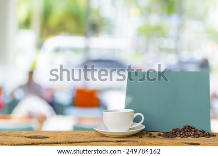 White cup of coffee and green chalkboard menu on wooden bar with blur image of people sit in living room .