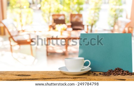 White cup of coffee and green chalkboard menu on wooden bar with blur image of  in living room near the garden .