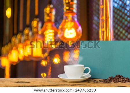 White cup of coffee and green chalkboard menu on wooden bar with coffee shop  blur light bulb background with bokeh image.
