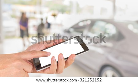 male hand is holding a modern touch screen phone and blur image of Commercially cars stand in show room of car shop.