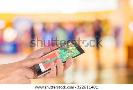male hand is holding a modern touch screen phone and Blurred image of people walking at shopping mall , blur background with bokeh