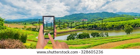 male hand is holding a modern touch screen phone and image of  field at Boon Rawd Farm is one of the largest tea produce in Thailand ,Chiang Rai