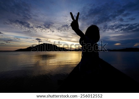 Silhouetted excited and joyous young girl showing peace hand sign with sunset background