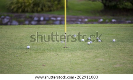 Golf balls in practice hole with flag marking the hole