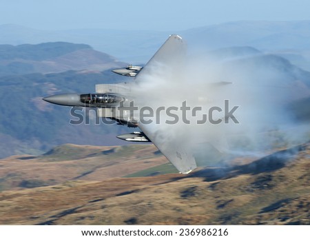 December 2014. Boeing F-15E Strike Eagle seen low level through the Bwlch Exit, Machynlleth Loop, LFA 7, Wales. The supersonic jet pours moisture off the wings as it pulls positive \'g\'.