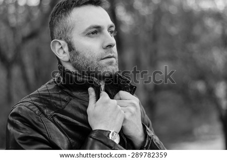 Stylish bully concept. Portrait of brutal young man with short wet hair wearing black jacket and posing over urban background. Hipster style. Close up. Black and white outdoor shot