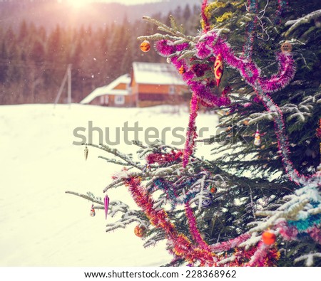 Close up detail of a decorated Christmas tree with bar balls in the wilderness nature of the snow mountains with a wooden house during Xmas winter season day on the sunset. Instagram style filter.
