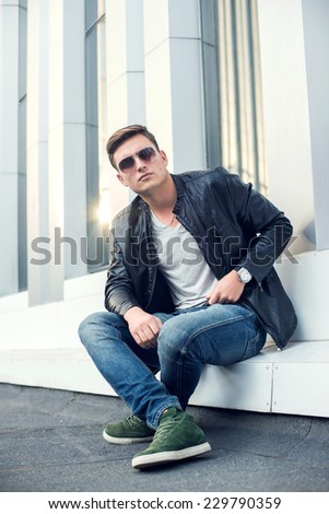 Young, fashioned man in black leather jacket, sunglasses and jeans. Outdoor portrait