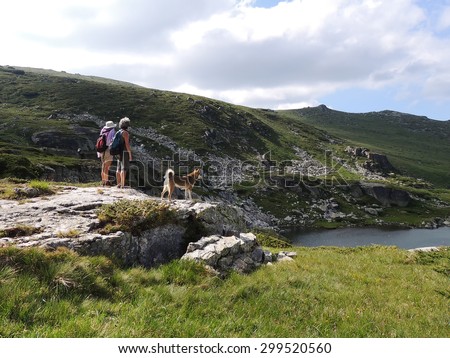 Two women and a West Siberian Laika Dog admiring a mountain lake