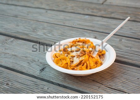 Paper plate with bolognese pasta on wooden background