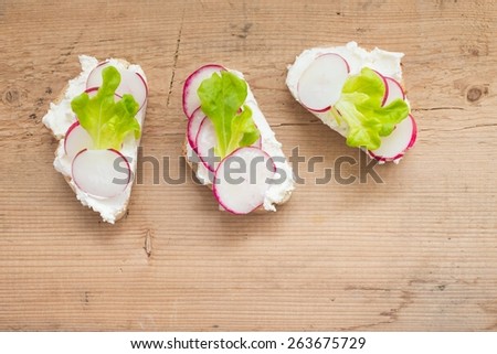 Three toasts with radish and cream cheese on wooden background, from above