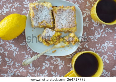 Lemon tarts on a plate, yellow cups and raw lemon on patterned l