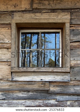 Closeup of an old rustic cabin's window reflecting wilderness