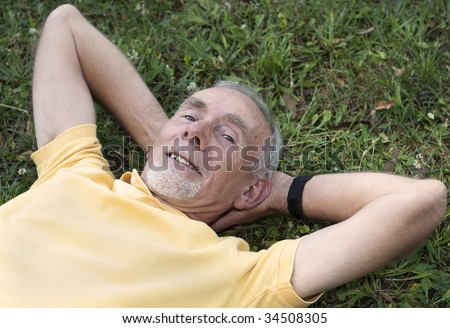 Old man lying down in grass, smiling, looking up at camera. Focus on face.