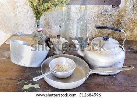 Old kitchen utensils in aluminum. Hanging from old wooden beams, pans, strainer, kettle: pans, sieve, kettle, coffeepot and three bottles