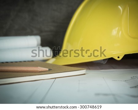 Pencil on architectural blueprint of office building over blurred Safety yellow hat and blueprint