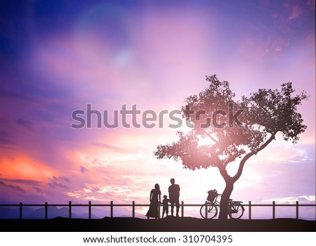 Silhouette of a happy family of four people, mother, father, baby, and child, and bicycle in front of a sun sky