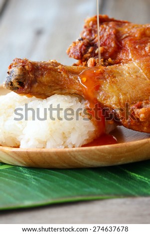 Thai style deep fried chicken thigh served on wooden plate with sweet chili sauce pouring on top