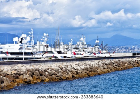 Luxury yachts anchored by a rocky pier in marina in South of France on a sunny summer day