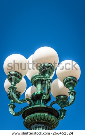 Old wrought iron lamp post with bulb lights and bright blue sky
