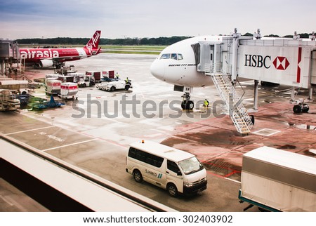 SINGAPORE AIRPORT, SINGAPORE - DECEMBER 6, 2014: Boeing 777 300 ER with HSBC passenger tunnel and Air Asia airplane standing on wet Singapore airport ground after rain - passenger terminal window view