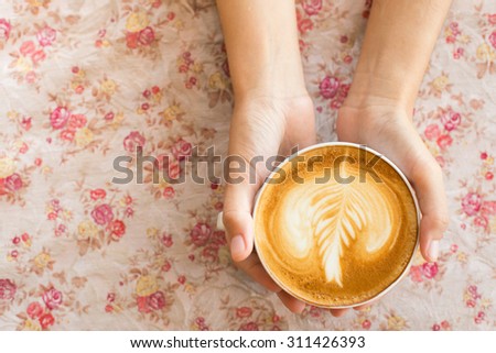 Vintage woman hands holding latte art coffee mug on flower vintage background