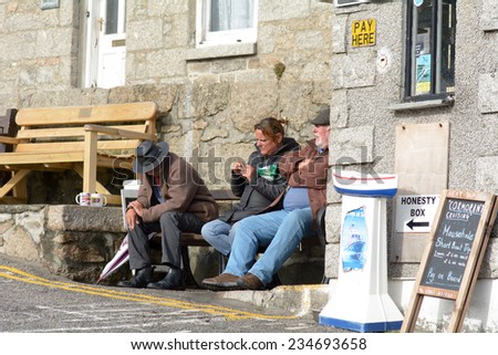 MOUSEHOLE, CORNWALL, ENGLAND - OCTOBER 2014: Men and woman sitting on bench smoking and drinking tea in the afternoon sun, shown on 24 October 2014 in Mousehole