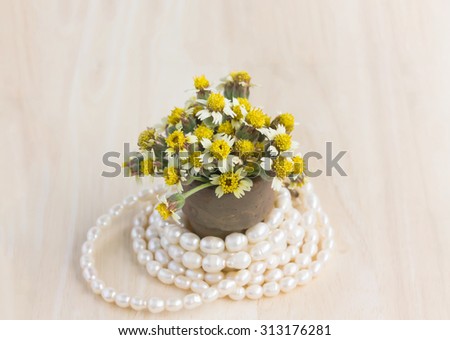 mini vintage style of little lovely yellow wild flower on wood table decorated with pearl necklace
