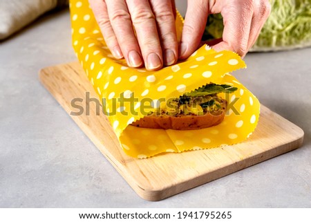 Woman hands wrapping a healthy sandwich in beeswax food wrap and cotton bag