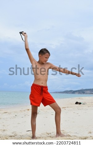 A boy in orange shorts against the backdrop of the beach and the sea swung and prepared to throw a knife at the target. Сток-фото © 