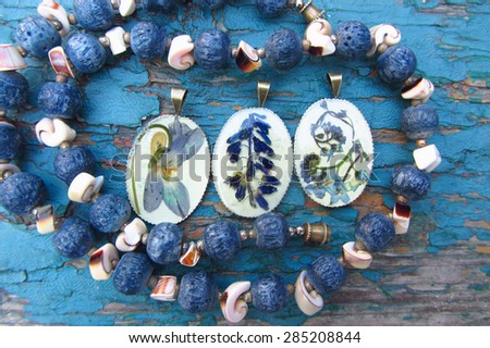Handmade women blue necklace of ceramic beads and pendant with flowers in resin, isolated on a grunge wooden background.