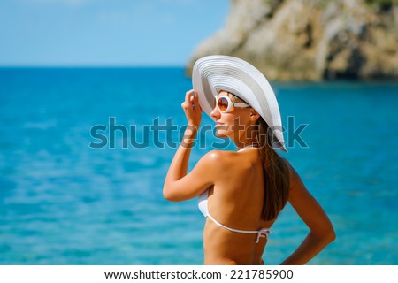 Sexy beautiful woman in white bikini and hat with creative white sunglasses on Mediterranean sea coast