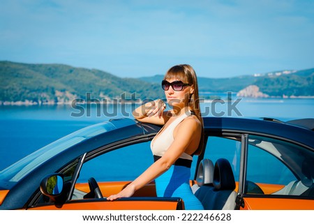 Beautiful young woman with long hair with orange cabriolet at the Mediterranean sea coast
