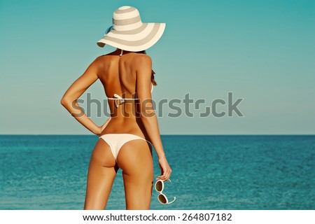 Sexy back of a beautiful woman in bikini on sea background. Sexy buttocks. Retro vintage toned image, film simulation.