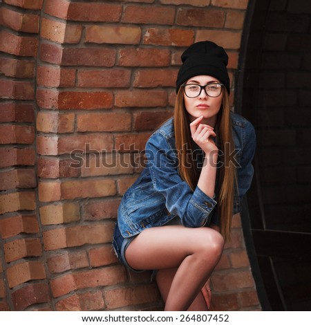 Young sexy hipster woman wearing jeans jacket, hipster black hat and glasses. Lifestyle city portrait.