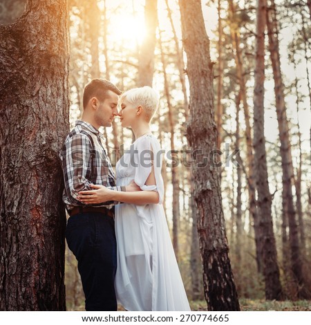Outdoor lifestyle portrait of young couple hugging in pine forest. Sunny warm weather. Backlight and sun. Retro vintage toned image, film simulation.