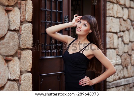 Outdoor lifestyle portrait of pretty young girl posing near old vintage wall and door, wearing in black dress on urban background.  Creative gel polish manicure.