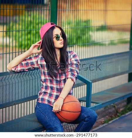 Outdoor lifestyle portrait of pretty young sitting girl, wearing in hipster swag grunge style with basketball in urban background. Retro vintage toned image, film simulation.
