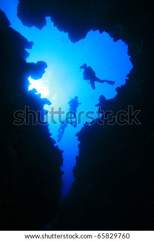 Scuba Divers descend into underwater cavern, silhouetted against sun