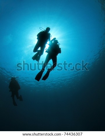 Scuba Divers swim together in blue ocean, silhouette against sunburst