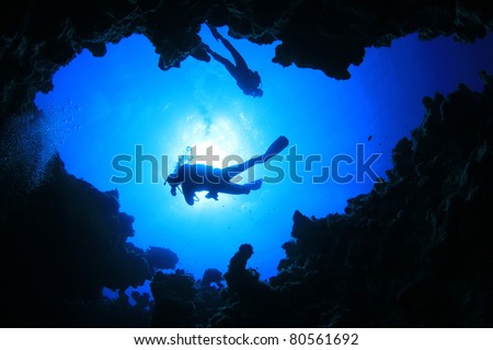 Scuba Divers descend into an Underwater Cavern. Silhouettes against sunburst