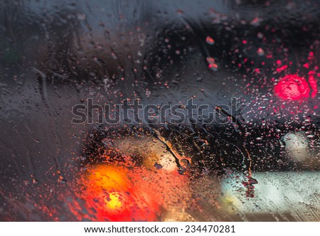 Blurry car silhouette seen through molten snow and water drops on the car windshield