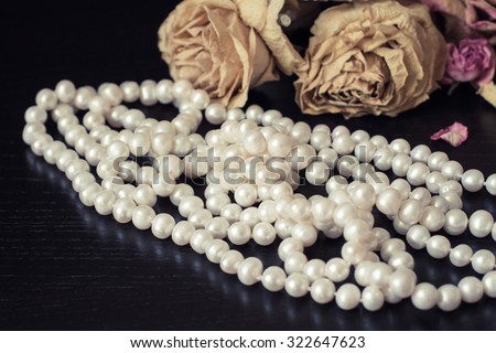 Vintage still life with faded roses and white pearls necklace close up