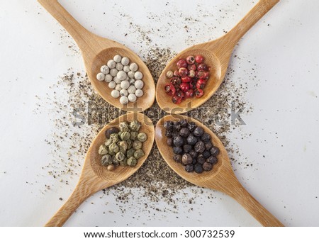 Pepper mill on a white isolated background with peppers green, red, black and white pepper next to the wooden spoon