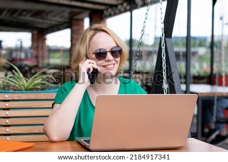 Happy girl talking on the phone with friends, browsing laptop in a street cafe. Happy girl working remotely in the park, using a laptop, reading social media internet shopping online Photo stock © 