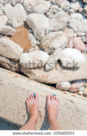 Overhead photo of feet on a background of big beach stones. Women feets view from above. Exploring, travelling, tourism, leisure.