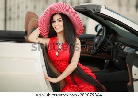 Fashionable young woman in car smiling girl in hat summer portrait beautiful female in red dress outdoors, sexy fashion woman model in luxury car, soft focus, series