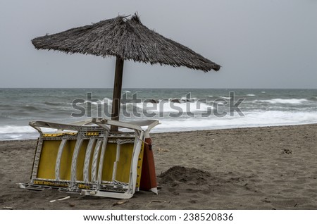 End of summer in Alcaidesa, Andalusia,Spain. Touristy place when the season is over. Sunbeds and umbrella left behind.  Abandoned beach equipment - summer is finished. Stormy weather, gray sky.