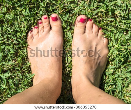 Feet on green grass with red nail polish on toes. Top view. Standing on the grass. Bare feet. No shoes. Tired feet.  Woman feet. Summer, warm weather, walking on grass, nature.