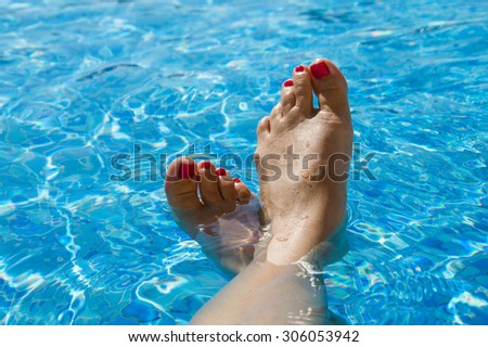 Feet in the swimming pool. Relax, vacation, summer. Red nails, suntanned skin, turquoise water. Sunlight dancing in the water. Summer holidays, relaxation, enjoyment, tanning. Floating on the surface